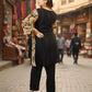 Woman in black outfit with floral sleeves standing on a street with shops in the background