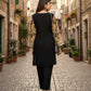 Woman walking down a cobblestone street in an old town, wearing a black outfit with a patterned jacket.