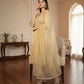 Woman in a beige traditional outfit standing in a well-lit room with wooden flooring and decorative elements.