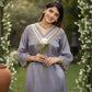 Woman in a light blue traditional outfit holding a flower, standing in a decorated garden.