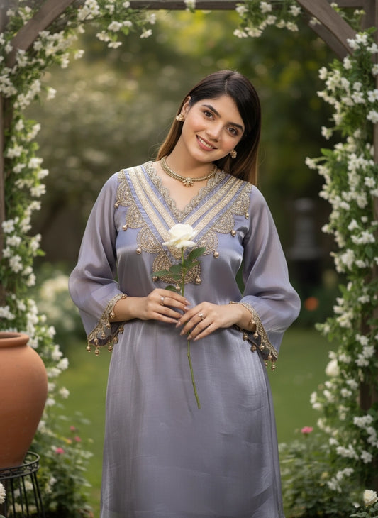 Woman in a light blue traditional outfit holding a flower, standing in a decorated garden.