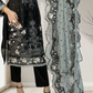 Black embroidered outfit with a sheer gray scarf held by a person indoors.