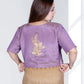 Woman wearing a purple blouse with gold embroidery and a beige skirt on a white background