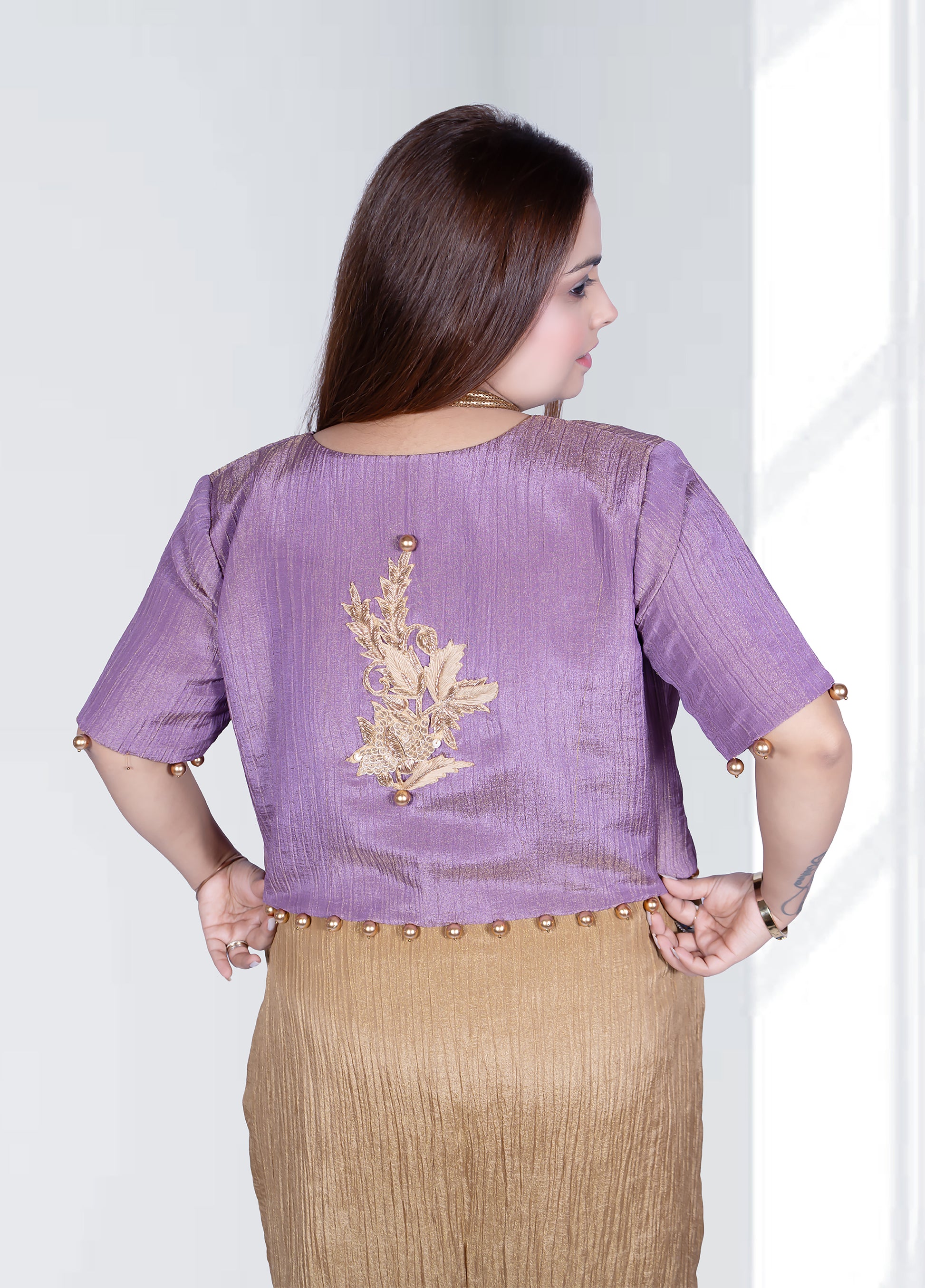 Woman wearing a purple blouse with gold embroidery and a beige skirt on a white background