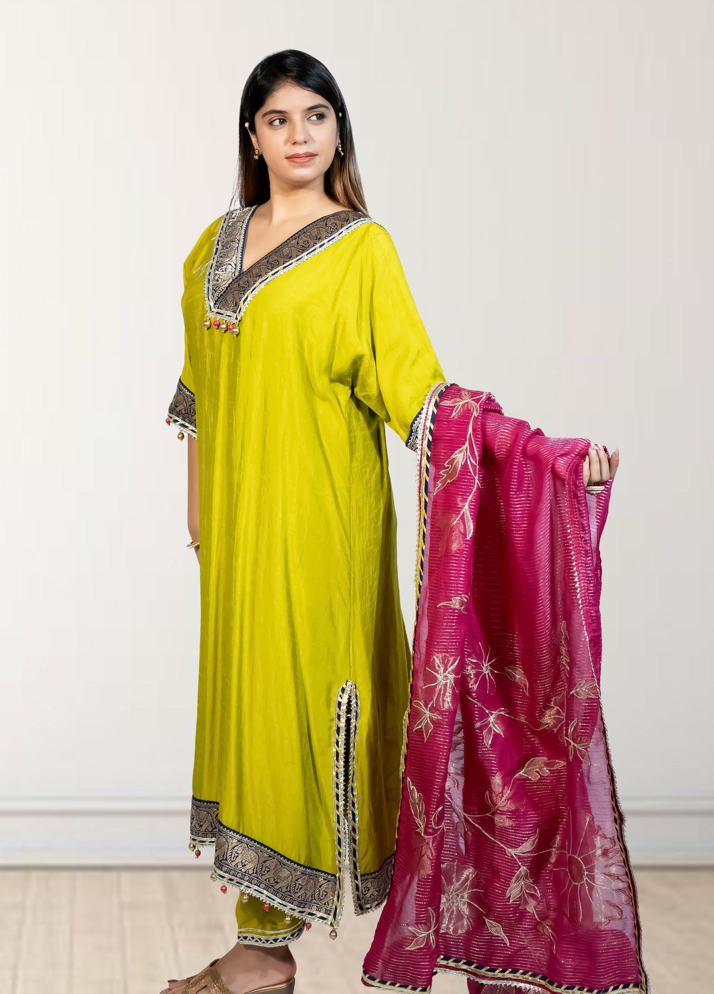 Woman wearing a green traditional outfit with a pink dupatta on a white background