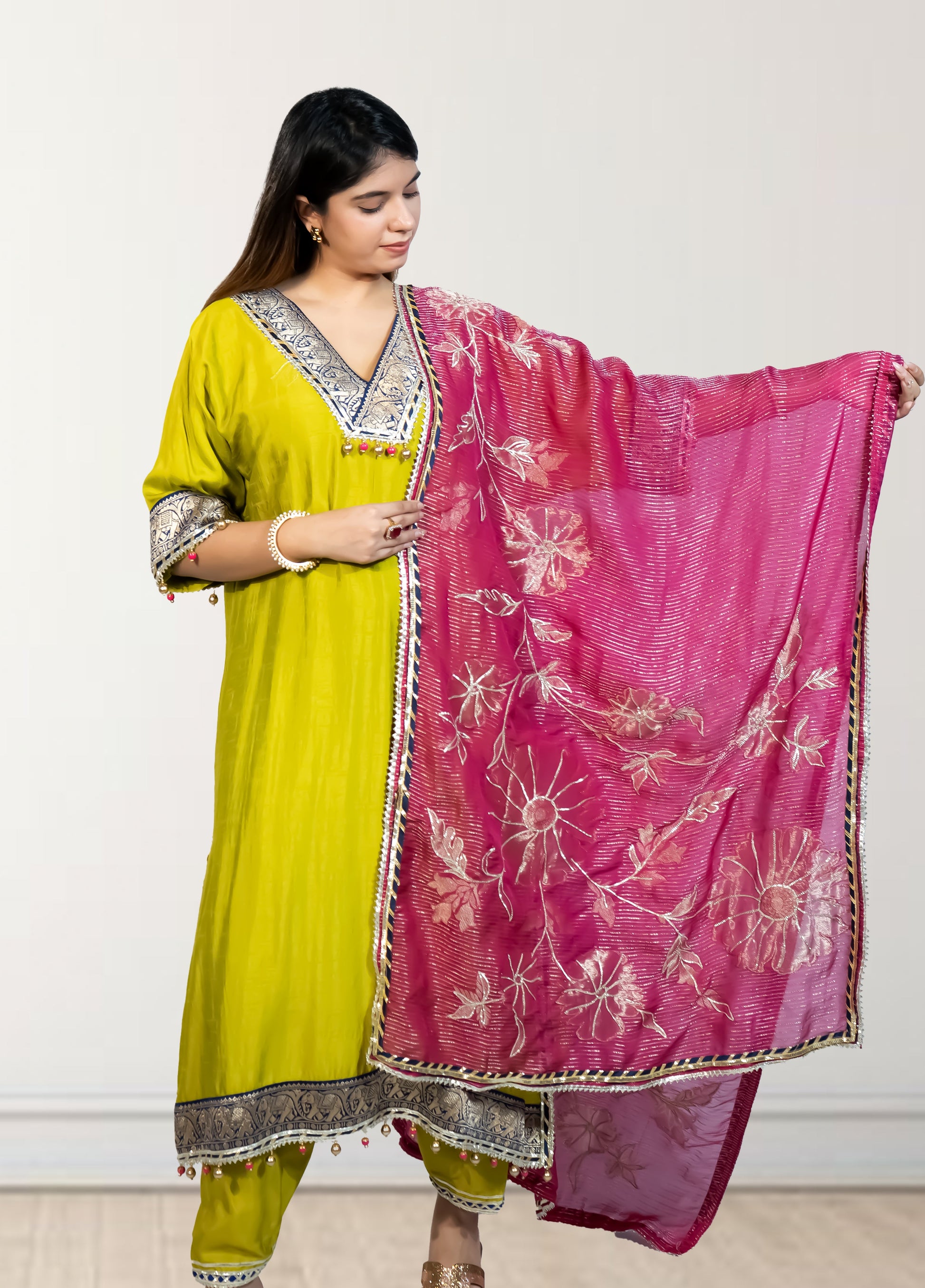 Woman wearing a yellow traditional outfit with a pink dupatta against a white background