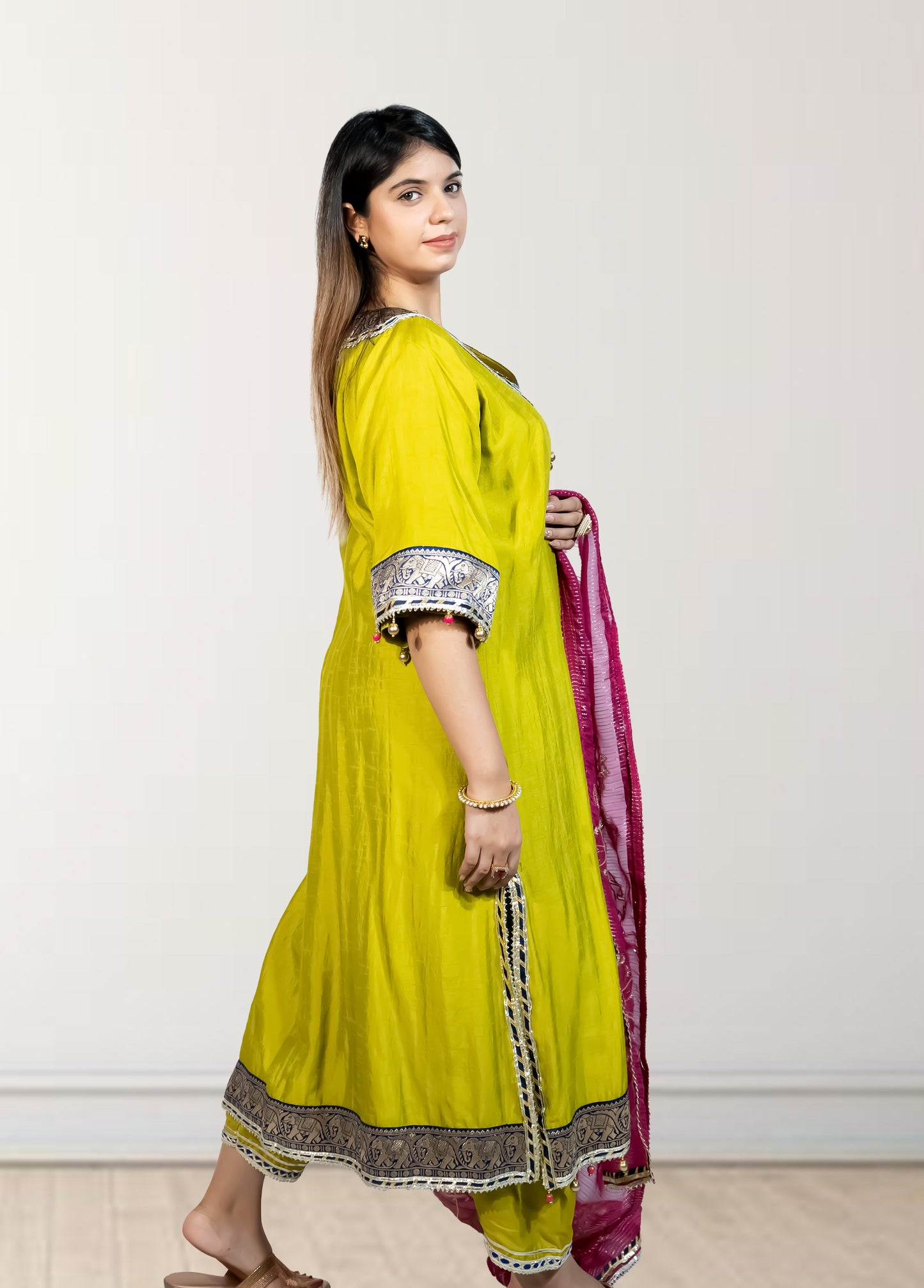 Woman wearing a bright yellow traditional outfit with a pink dupatta against a white background