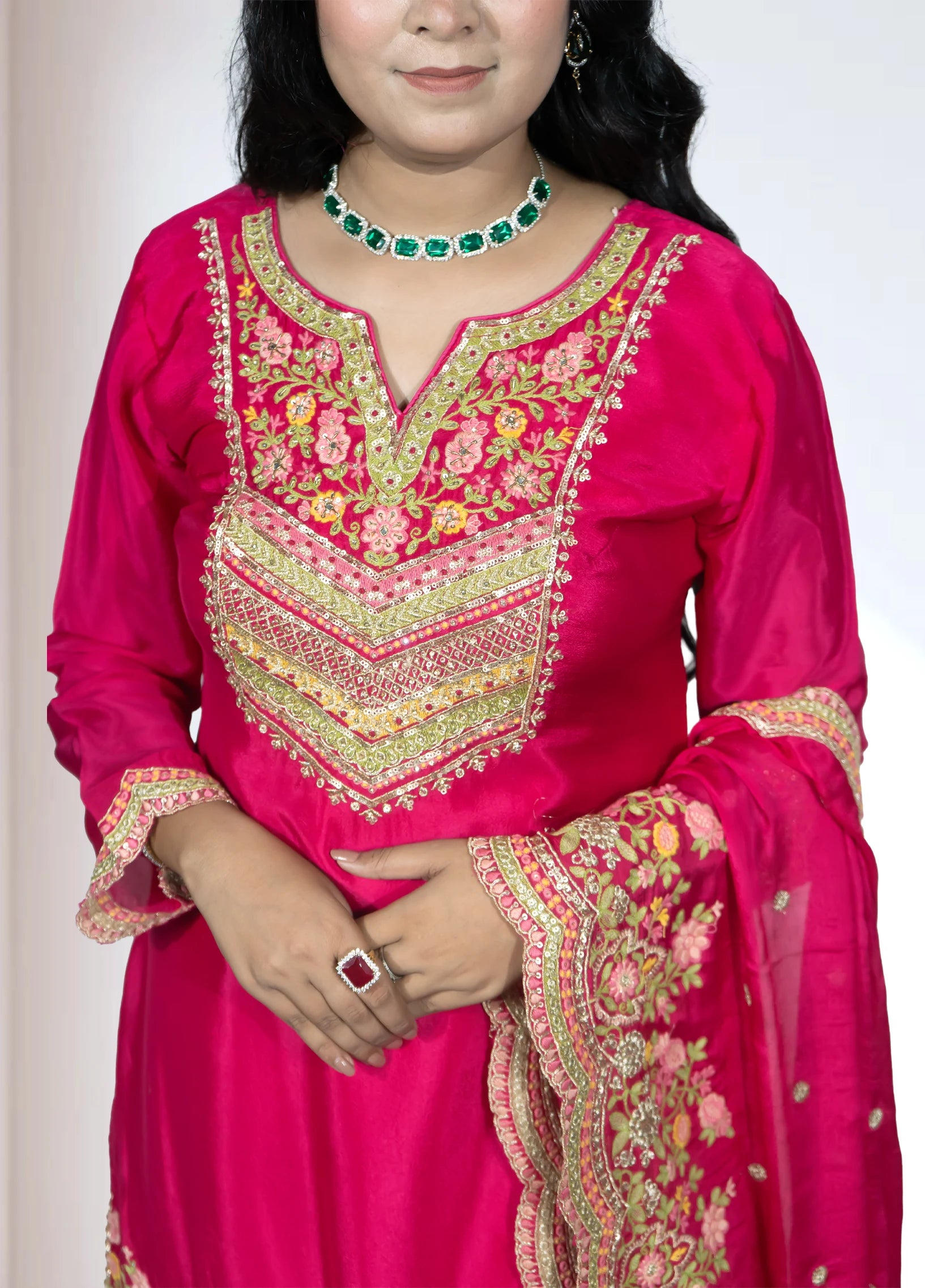 Woman wearing a bright pink traditional outfit with intricate embroidery on a plain background