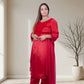 Woman in a red traditional outfit standing in a well-lit room with a plant in the background.