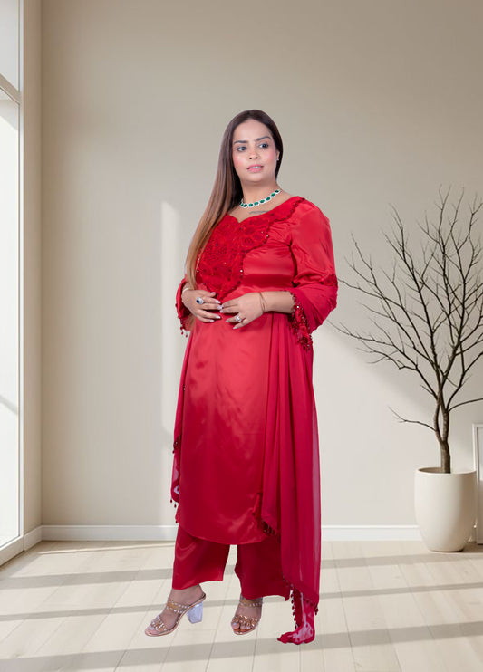 Woman in a red traditional outfit standing in a well-lit room with a plant in the background.