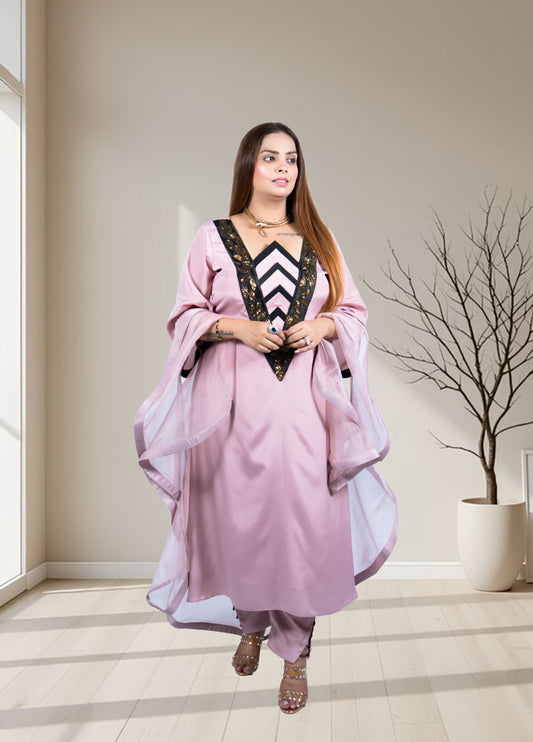 Woman in a pink traditional outfit standing in a well-lit room with a plant in the background.