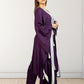 Woman wearing a purple outfit with a white and black scarf against a plain background