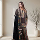 Woman wearing a patterned dress with a black dupatta in a room with a large window and a plant.