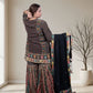Woman in traditional outfit holding a garment in a room with a window and plant.