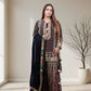 Woman wearing a traditional outfit with a patterned top and black dupatta in a minimalistic room.