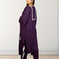 Woman wearing a purple outfit with white embroidery against a white wall.