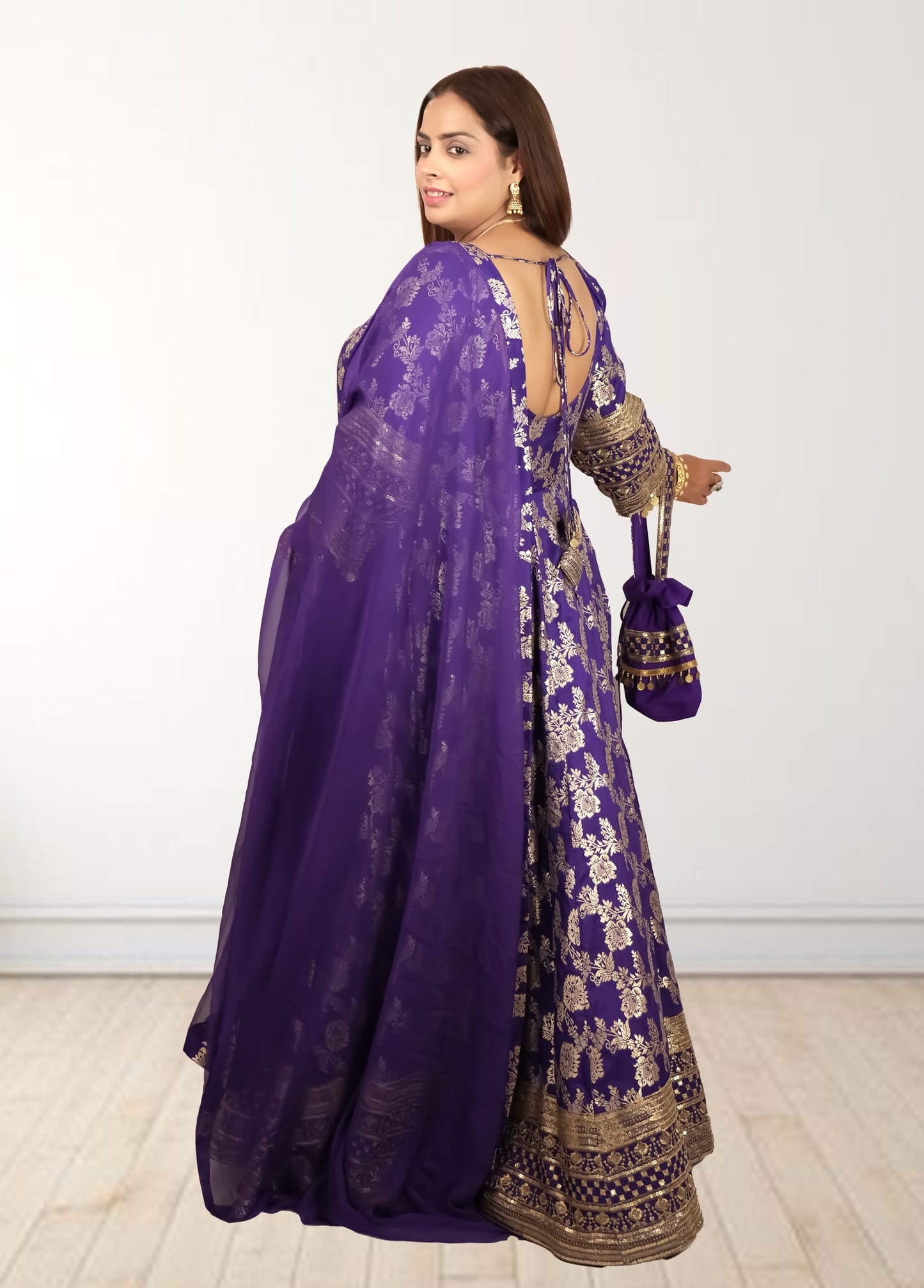 Woman wearing a purple saree with gold patterns on a white background