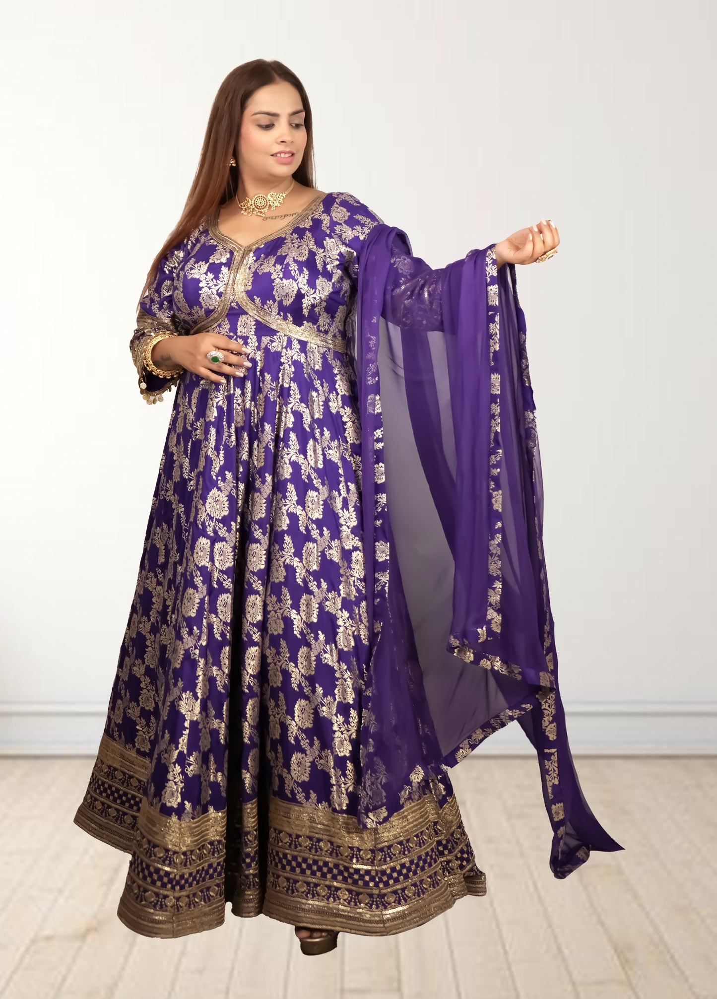 Woman wearing a traditional purple and gold outfit with a matching dupatta on a white background