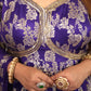 Person wearing a purple traditional outfit with gold embroidery, holding a small object.