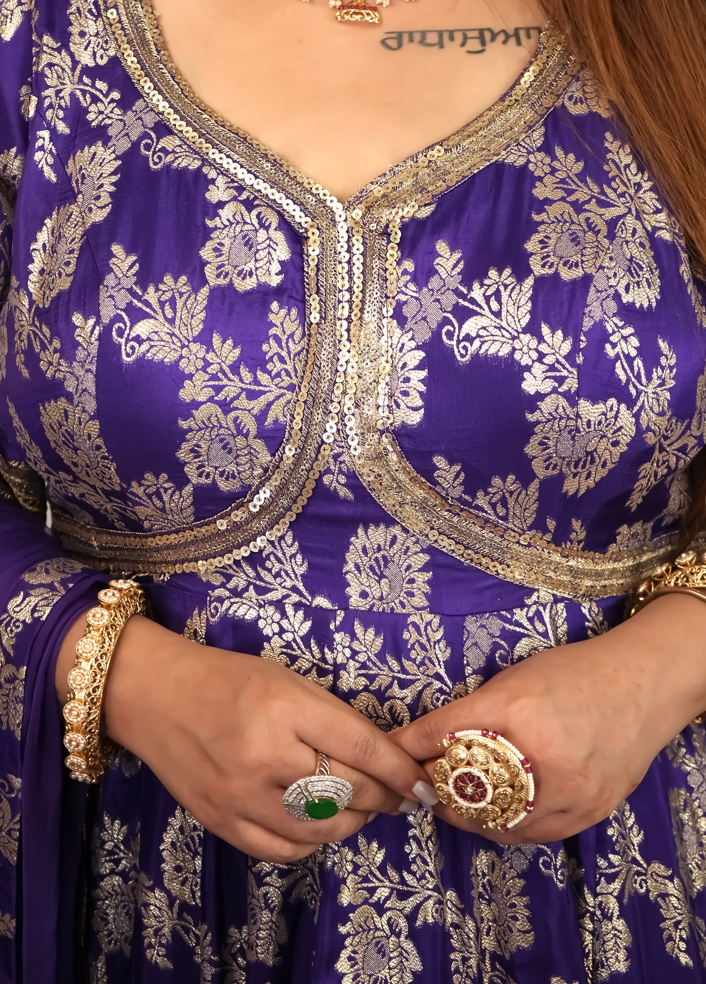 Person wearing a purple traditional outfit with gold embroidery, holding a small object.