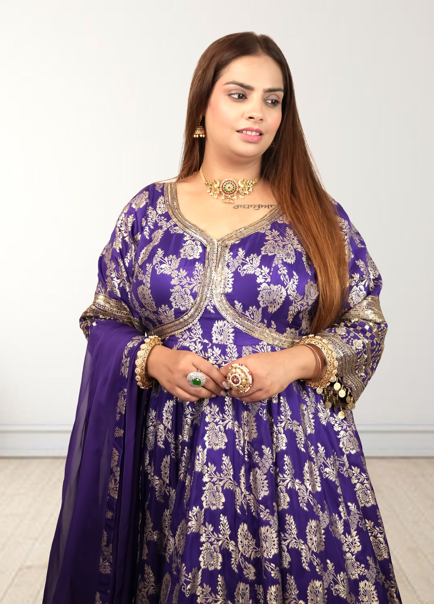 Woman wearing a purple embroidered traditional outfit with gold details on a white background