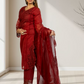 Woman wearing a red traditional outfit with a matching dupatta in a minimal indoor setting.