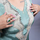 Teal outfit with intricate beadwork and jewelry on a plain background
