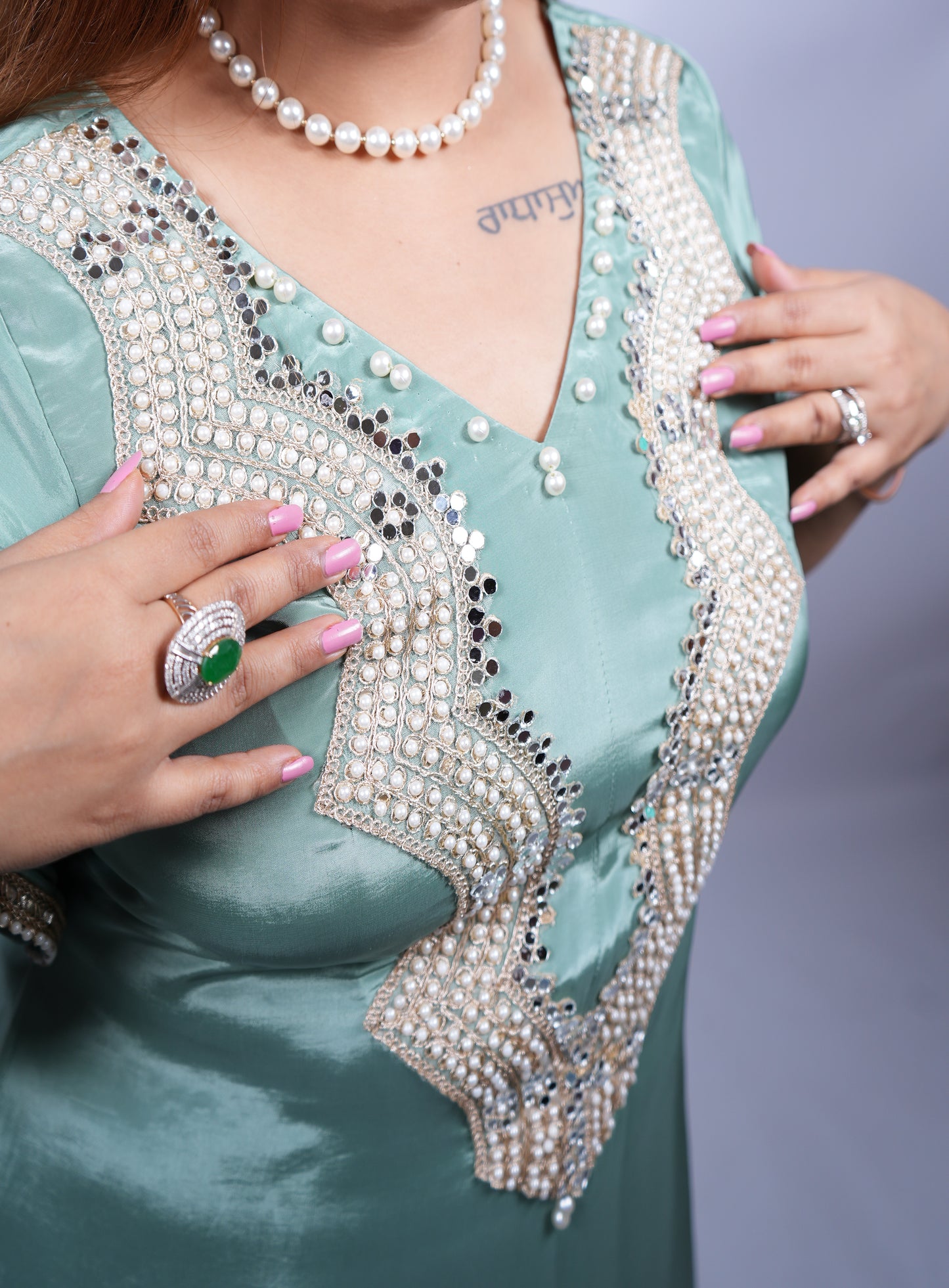 Teal outfit with intricate beadwork and jewelry on a plain background