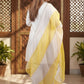 Woman in a white and yellow saree standing in a room with wooden paneling and plants.