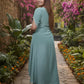 Woman in a teal outfit walking through a garden with pink flowers and stone path.