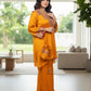 Woman in a mustard yellow traditional outfit with intricate patterns in a modern living room.