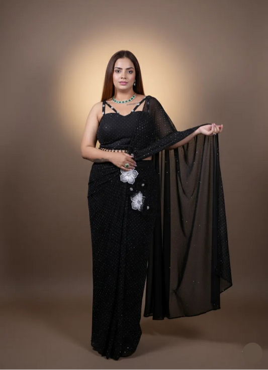 Woman wearing a black saree with a floral blouse against a brown background