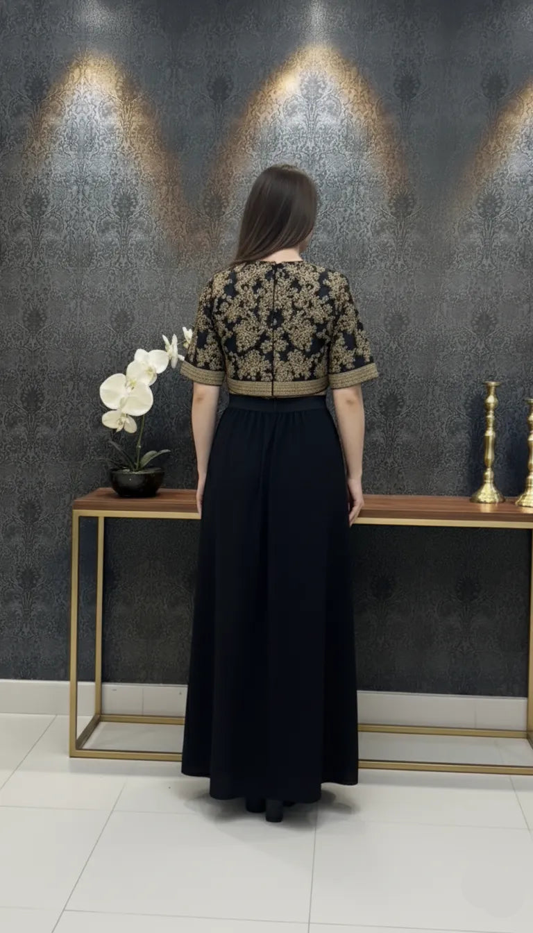 Woman in a black and gold outfit standing in front of a decorative wall with peacock feathers.