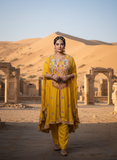 Woman in a yellow traditional outfit standing in a desert with ancient architecture.