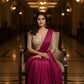 Woman in a pink saree sitting on a chair in an elegant hallway.