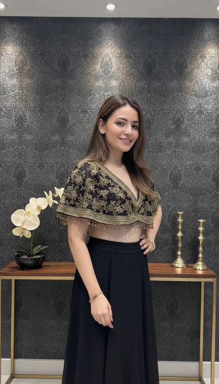 Woman wearing a black and gold top with a black skirt in front of a decorative wall.