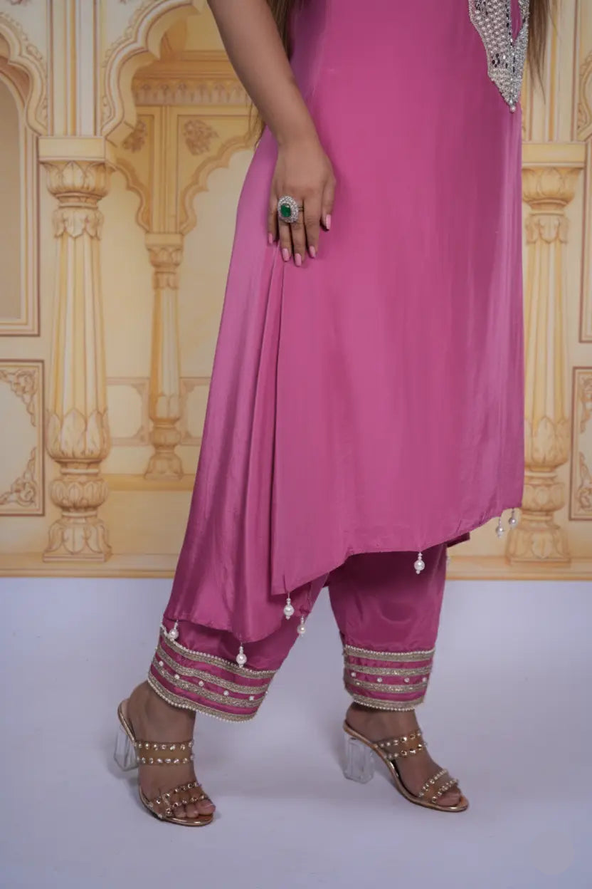 Person wearing a pink traditional outfit with embellishments against a decorative wall.