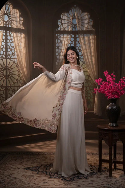 Woman in a white traditional outfit standing in a room with stained glass windows and a vase of pink flowers.
