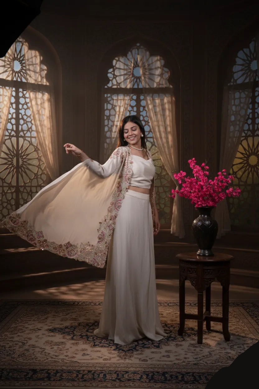 Woman in a white traditional outfit standing in a room with stained glass windows and a vase of pink flowers.