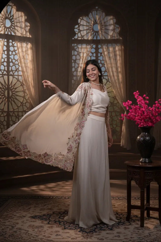 Woman in a white traditional outfit standing in a room with stained glass windows and a vase of pink flowers.