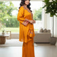 Woman in a mustard yellow traditional outfit standing in a modern living room.