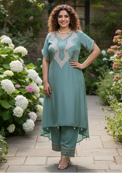 Woman in a teal outfit standing in a garden with flowers and a stone wall in the background