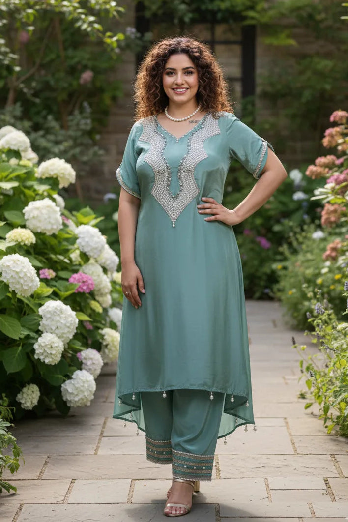 Woman in a teal outfit standing in a garden with flowers and a stone wall.
