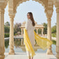Woman in a white and yellow traditional outfit standing in front of an archway with a pool and garden in the background.