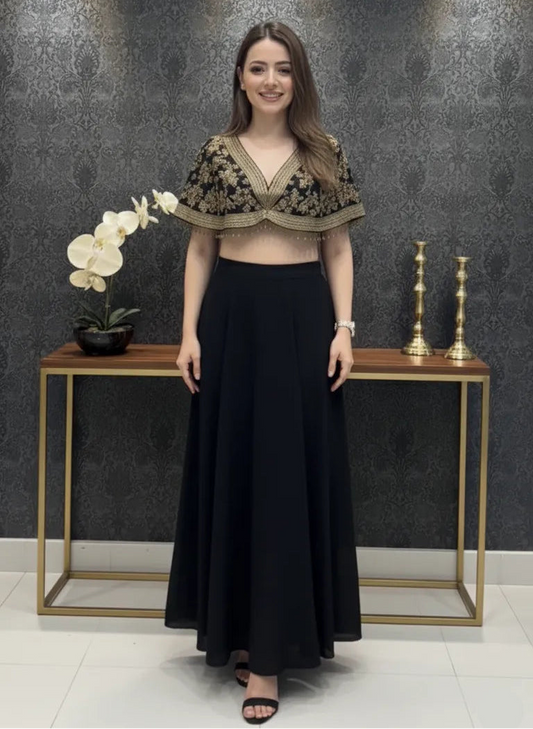 Woman in a black and gold outfit standing in front of a decorative wall with a small table and decor items.