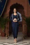 Woman in a navy blue traditional outfit standing in an ornate room with plants and decorative elements.