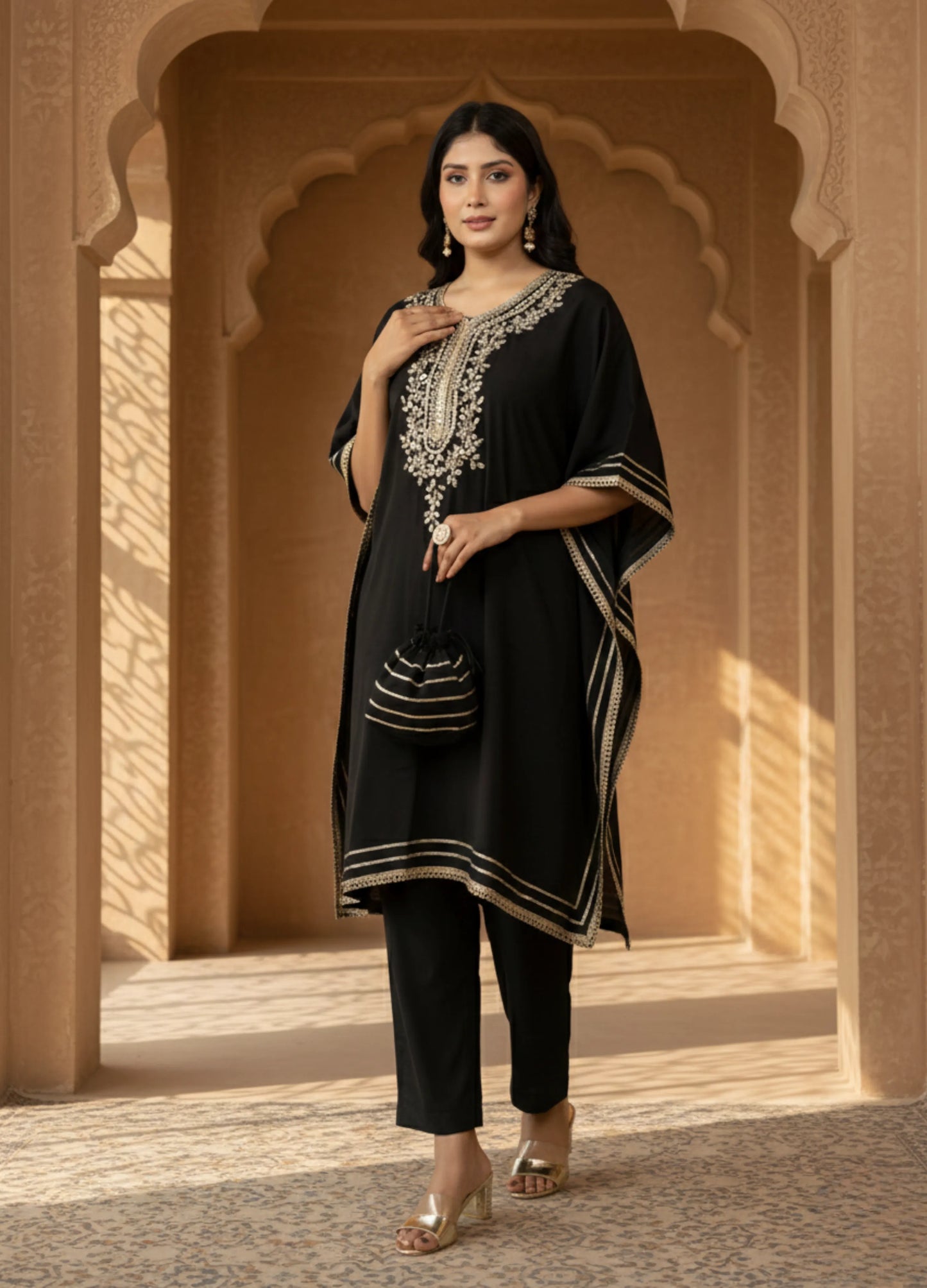 Woman wearing a black traditional outfit with intricate white embroidery in an architectural setting.