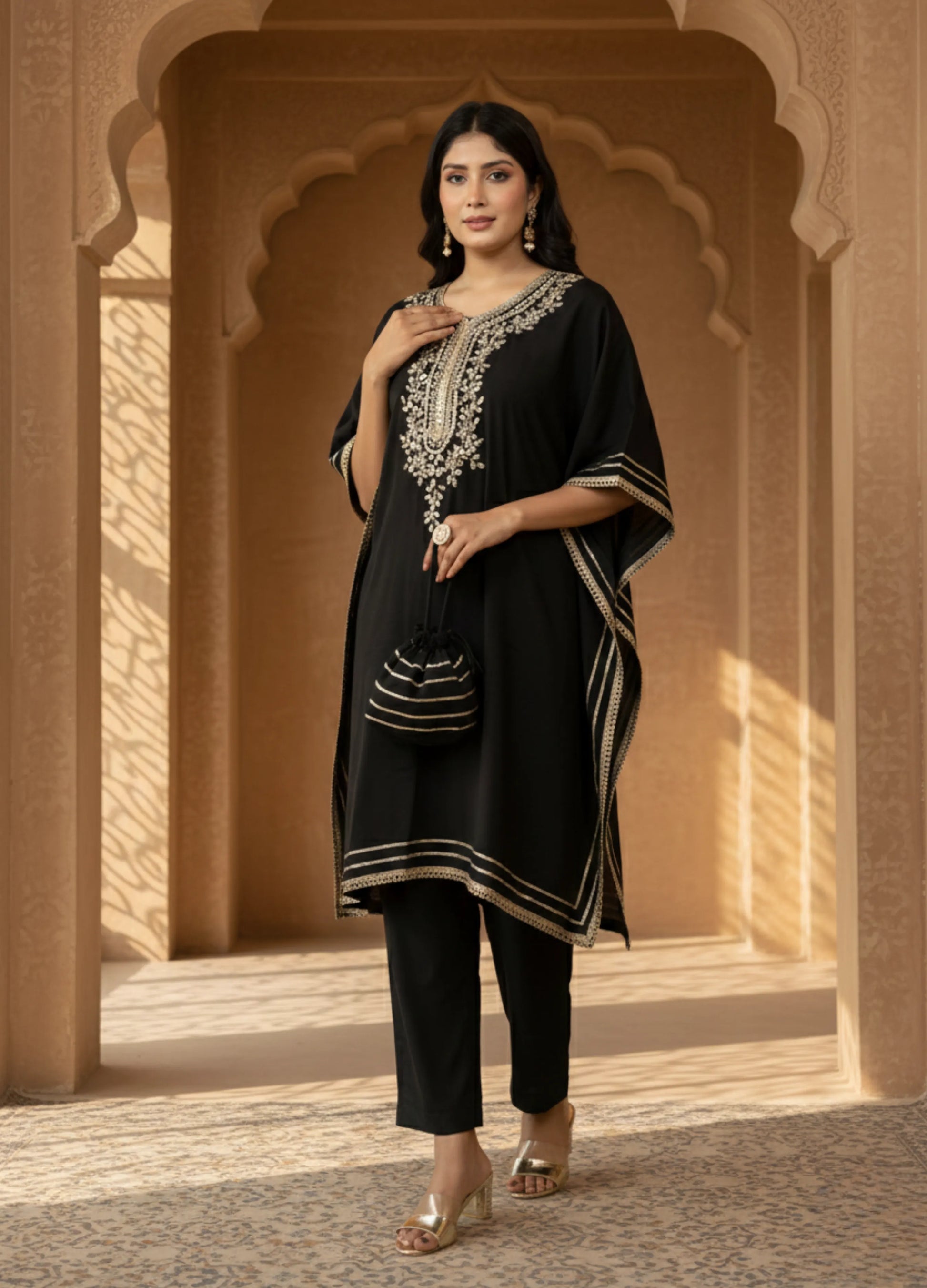 Woman wearing a black traditional outfit with intricate white embroidery in an architectural setting.