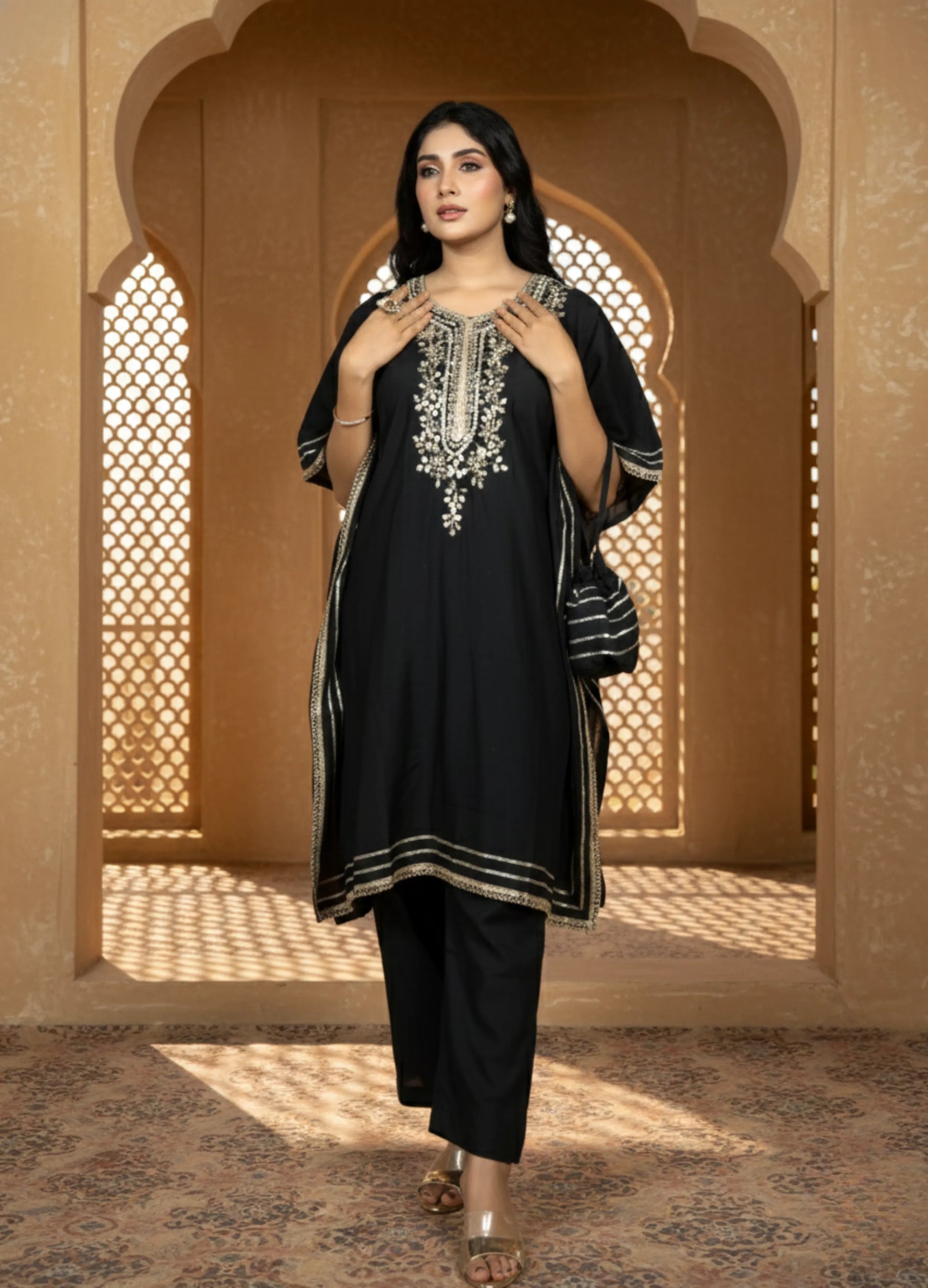 Woman in a black traditional outfit with embroidery standing in front of an arched window.
