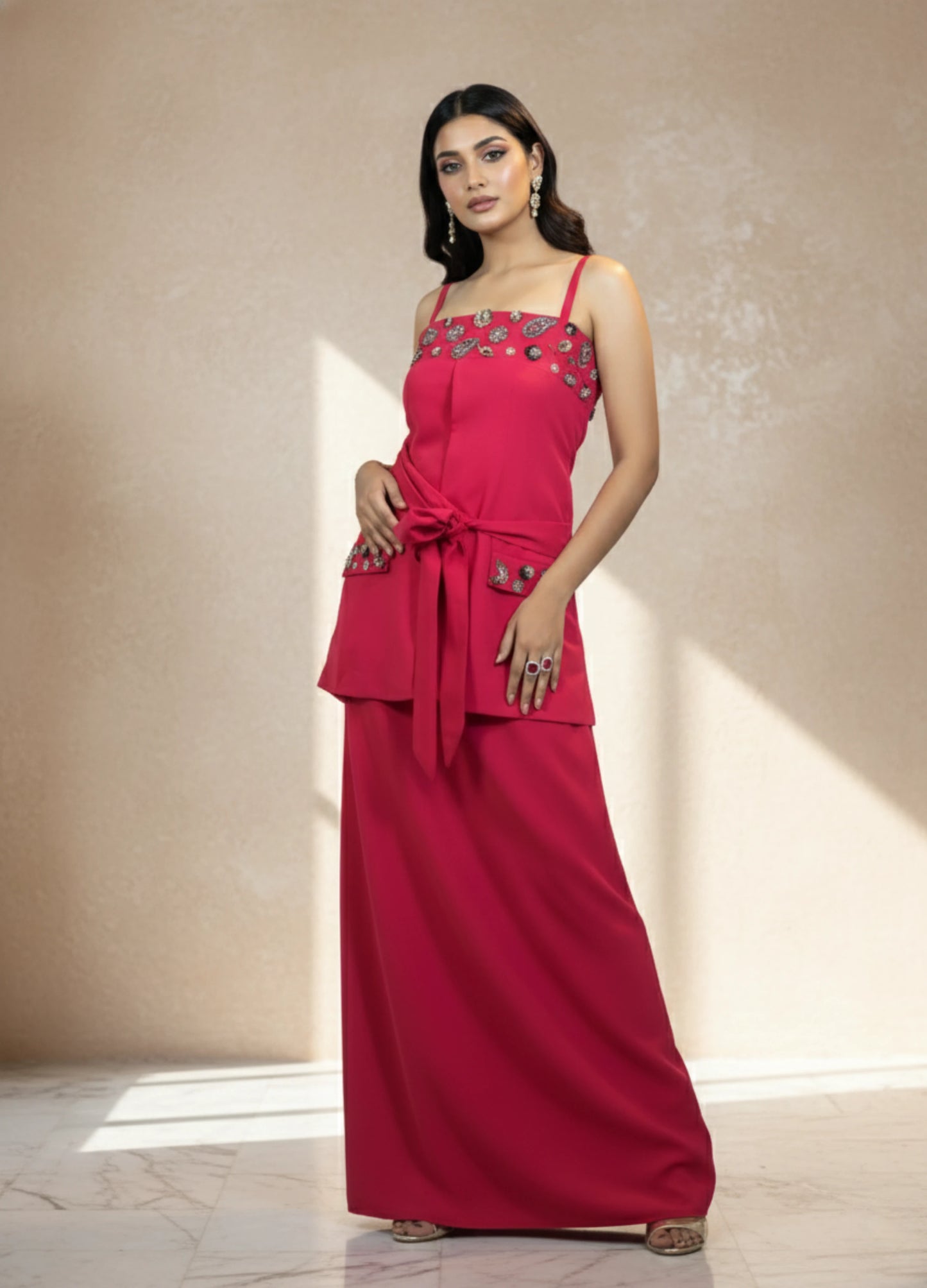 Woman wearing a red evening gown with floral embellishments in a neutral setting